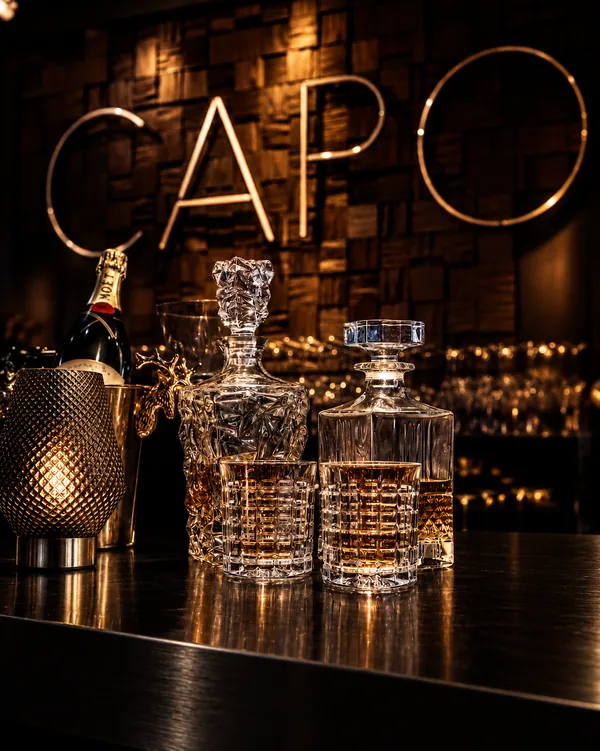 Kristallen karaffen, whisky en champagne aan de bar onder de CAPO-letters